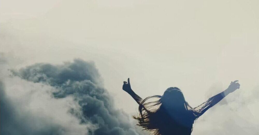 Strong woman with arms raised triumphantly in the sky among clouds, representing resilience and rebuilding life