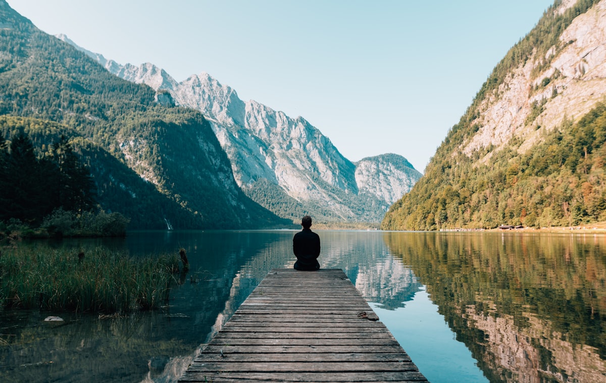5 Ancient Wisdom Practices That Science Has Now Proven Work 2 Woman sitting on a bench at sunset overlooking mountains, representing mindfulness and slowing down