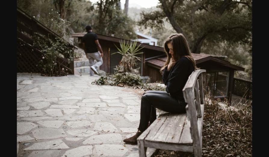Woman sitting alone on a bench looking down while a man walks away — signs of a toxic relationship